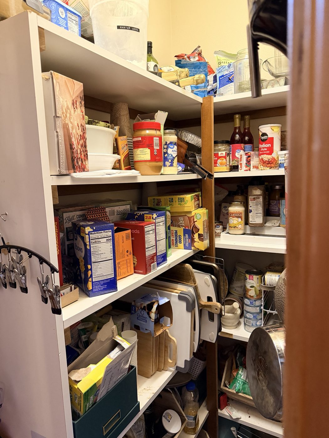 Pantry shelving stacked with mixed food, cookware and household items.